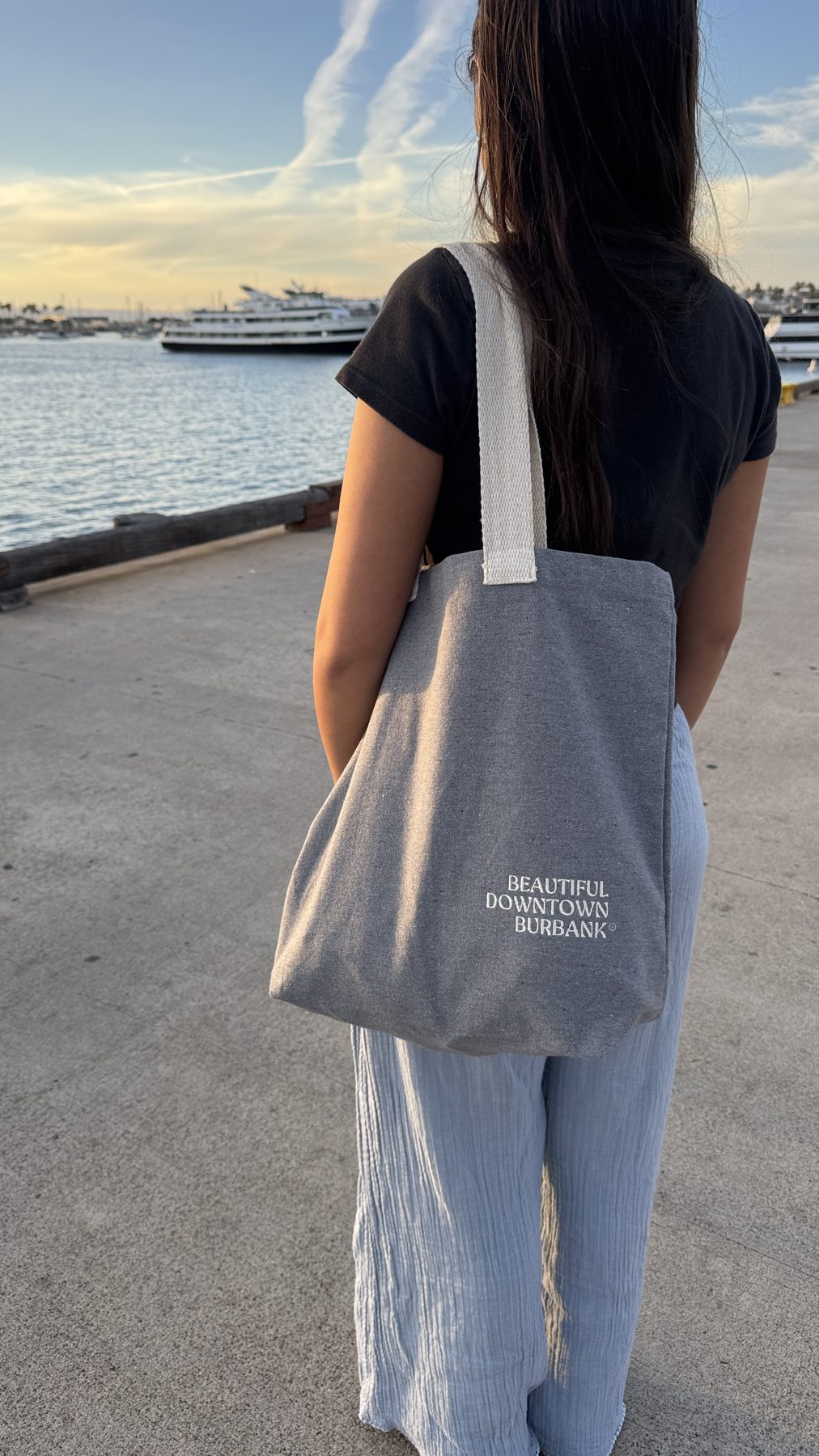 Woman by the harbor at sunset carrying a gray Beautiful Downtown Burbank tote