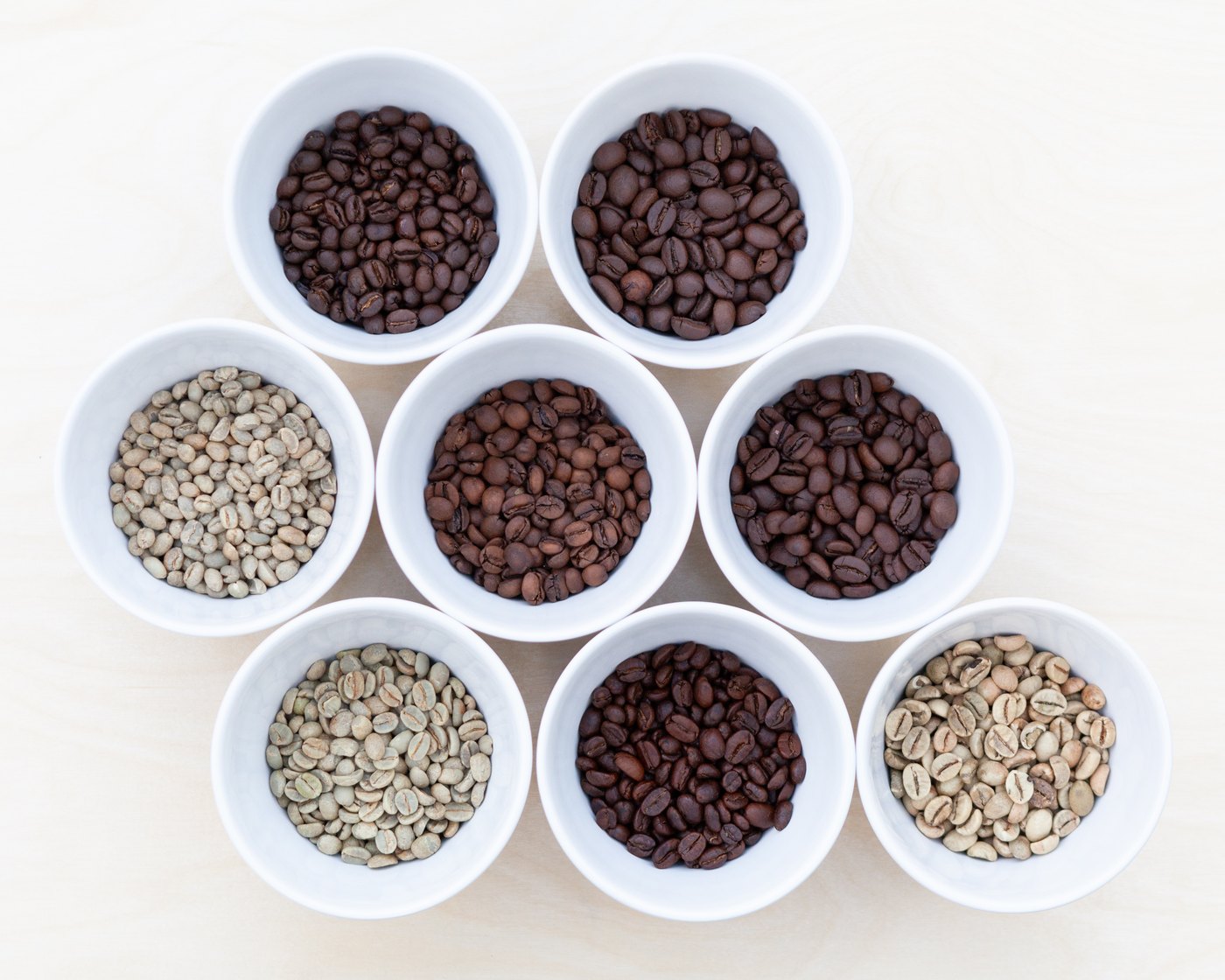 Green, light-roasted and dark-roasted coffee beans in white cups