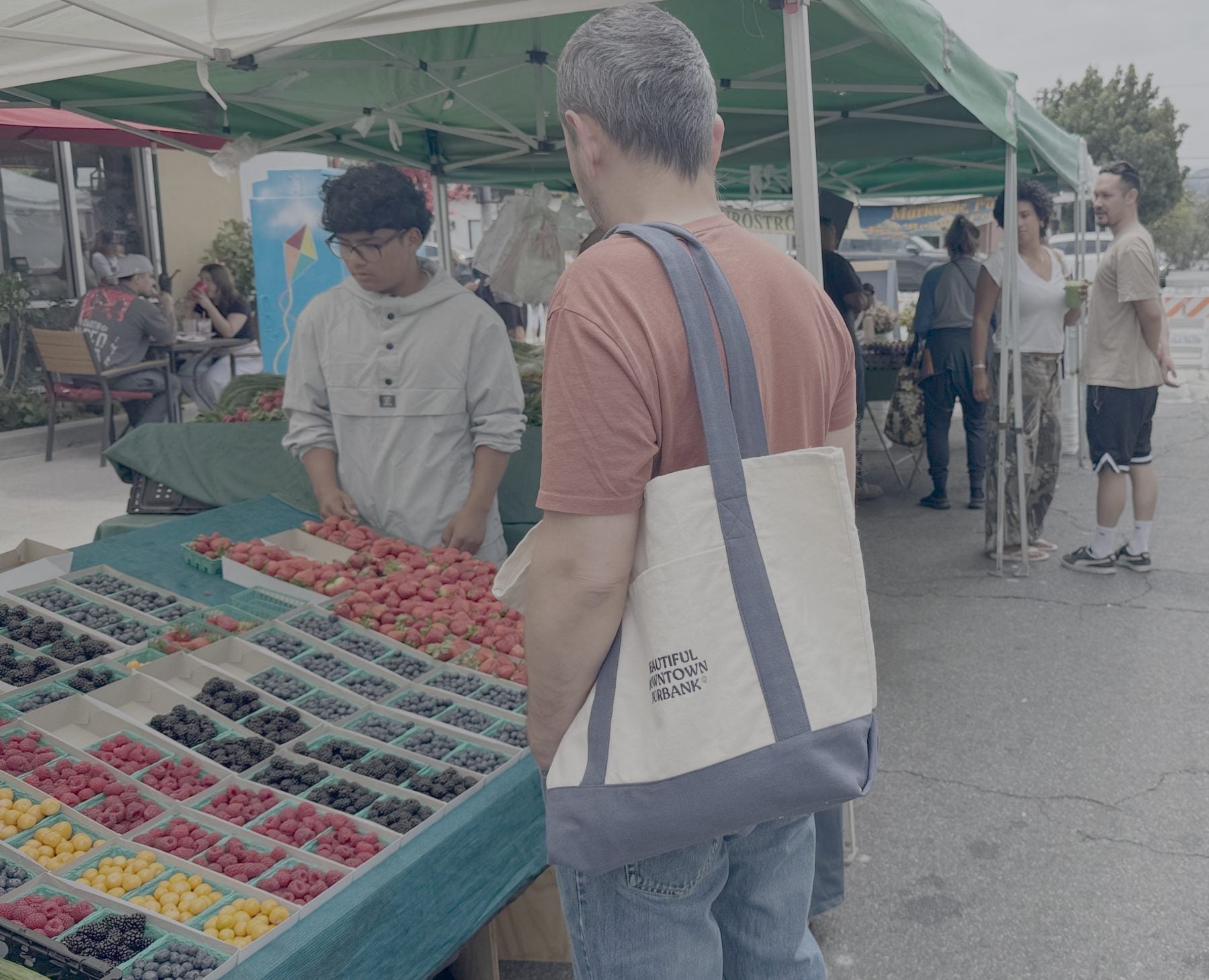 Shopper with a canvas Beautiful Downtown Burbank tote at a farmers market berry stand